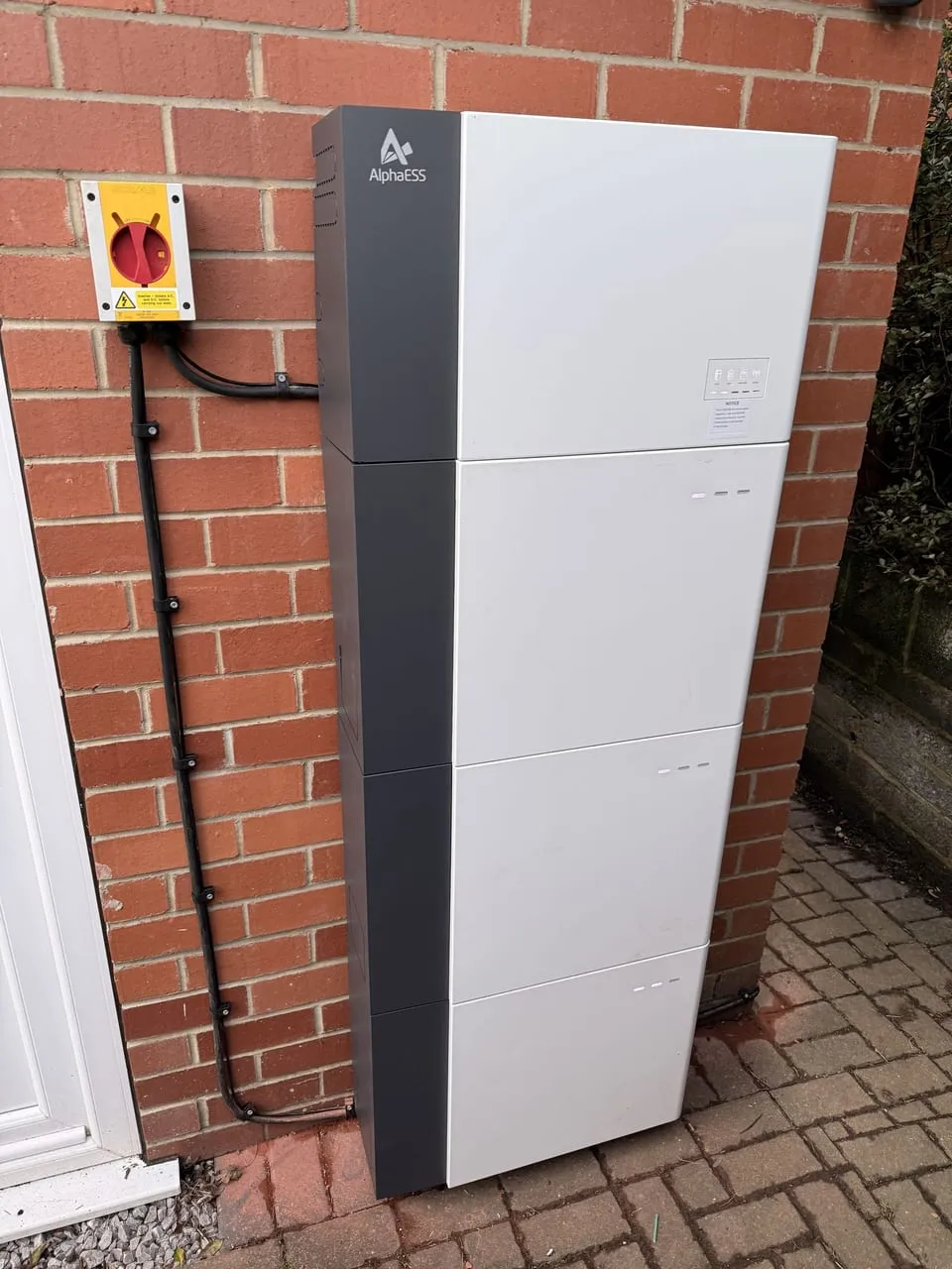 An AlphaESS home solar battery storage unit mounted on a brick wall