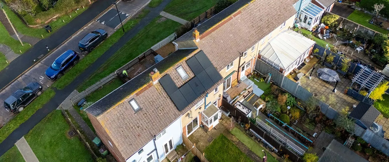 Aerial view of a UK terraced street with black solar panels and an installer on the roof